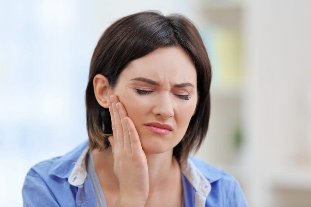 Woman holding her cheek in pain from toothache before seeing an emergency dentist